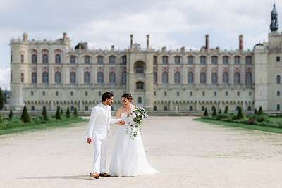 Les mariés marchent main dans la main en se chamaillant devant l'imposant château