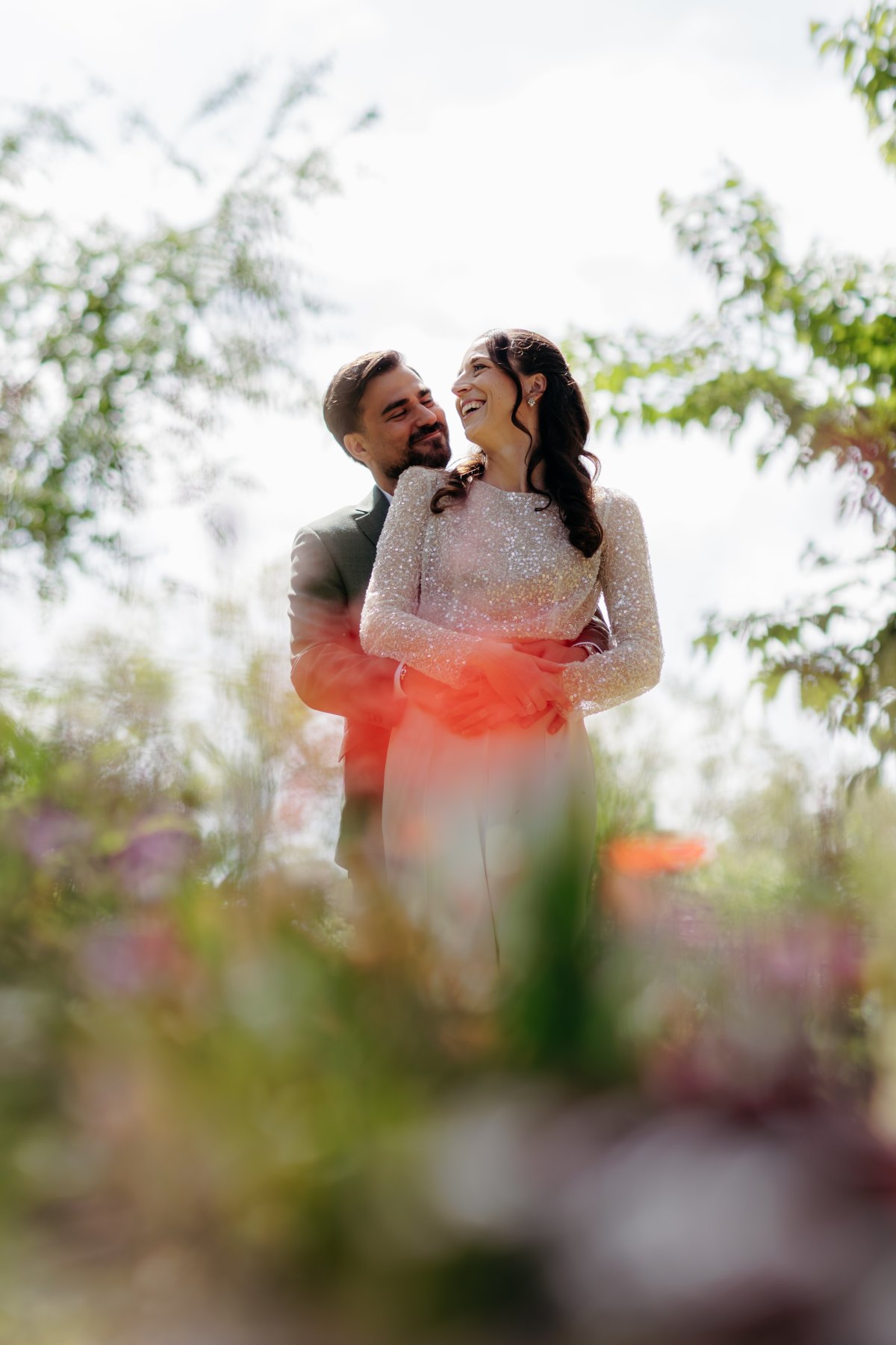 La mariée rit dans les bras du marié, derrière un rideau de fleurs